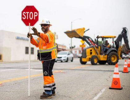 Traffic control officer holding a stop sign in a construction zone, with heavy machinery and traffic cones visible, emphasizing road safety and effective traffic management in Adelaide.