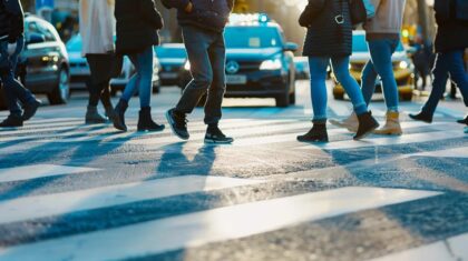 Pedestrians crossing a zebra crossing with vehicles in the background, emphasizing urban pedestrian safety and traffic management.