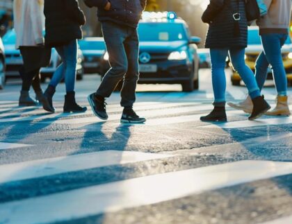 Pedestrians crossing a zebra crossing with vehicles in the background, emphasizing urban traffic management and pedestrian safety in construction areas.